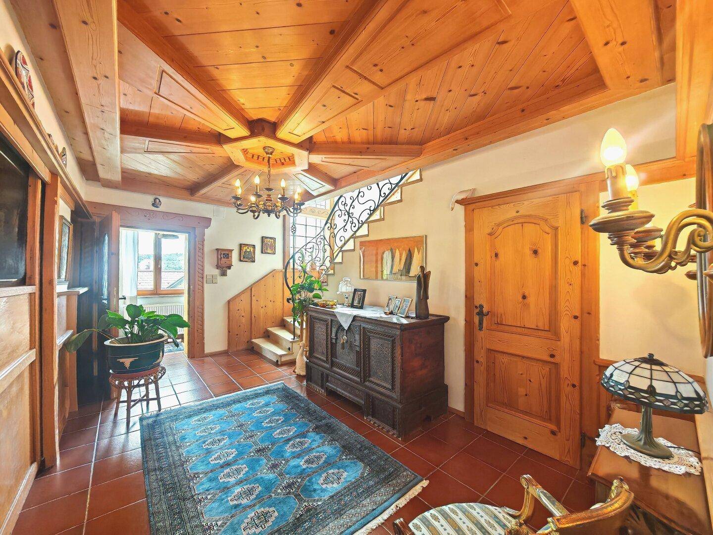 Geräumiger Flur mit beeindruckender Holzdecke, Fliesenboden, antiken Möbeln und geschwungener Treppe.