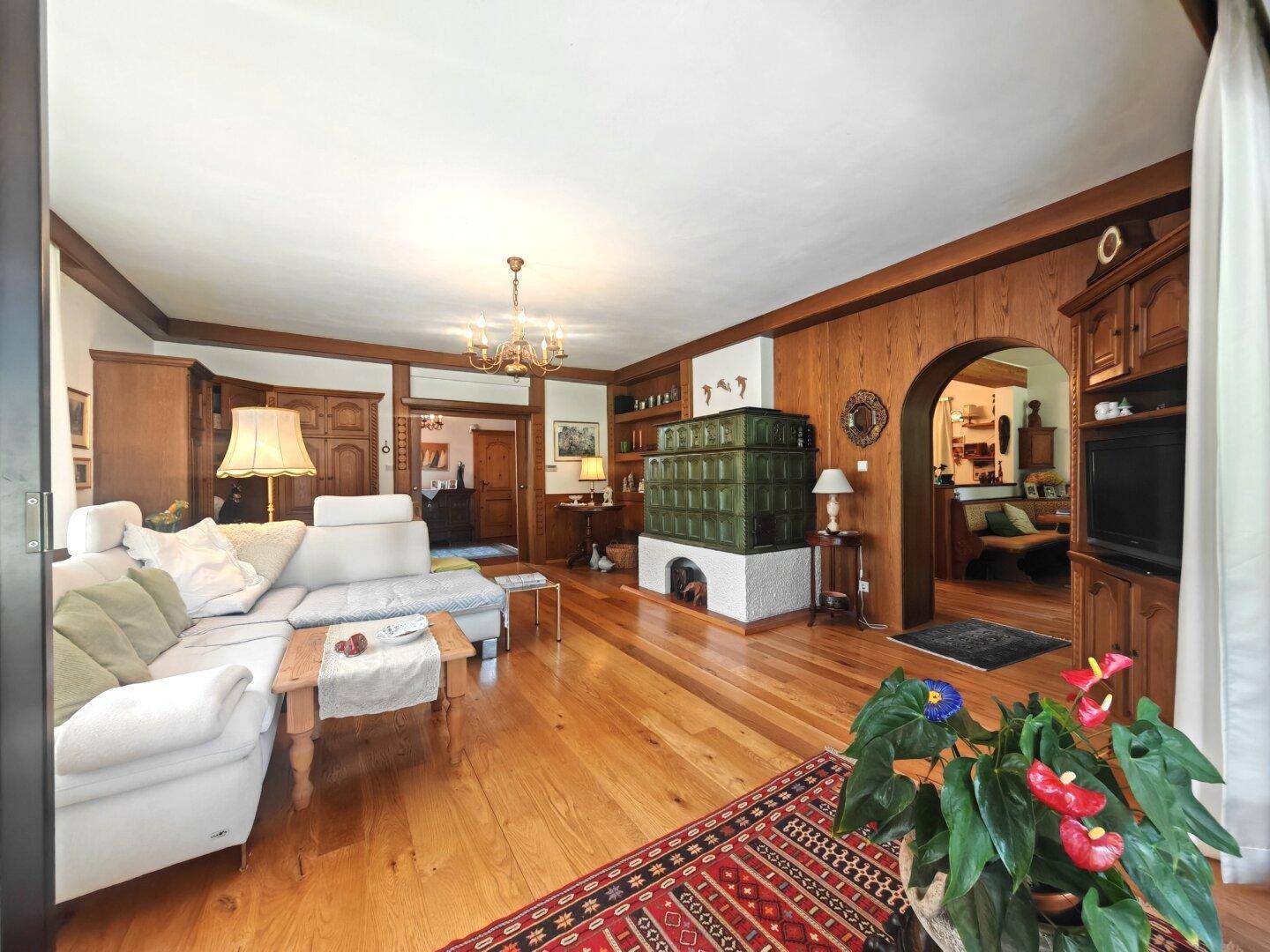 Gemütliches Wohnzimmer mit Holzboden, weißem Sofa und einem traditionellen grünen Kachelofen.