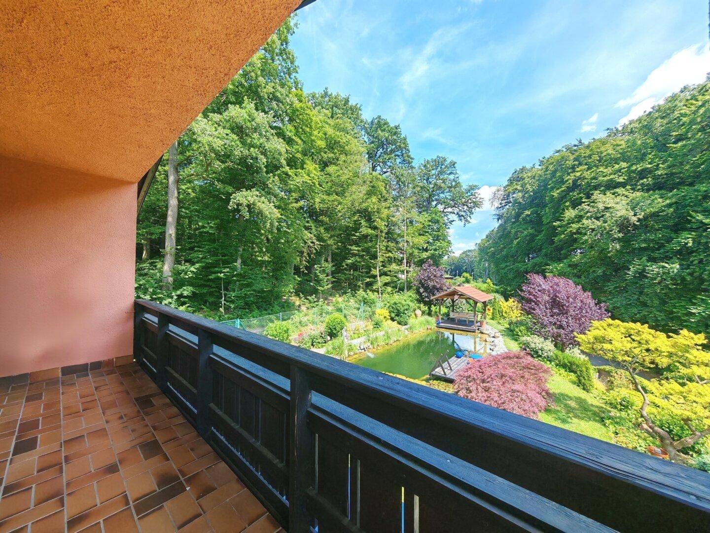 Geräumiger Balkon mit Fliesenboden und Holzgeländer, bietet einen herrlichen Blick auf den Garten und Wald.