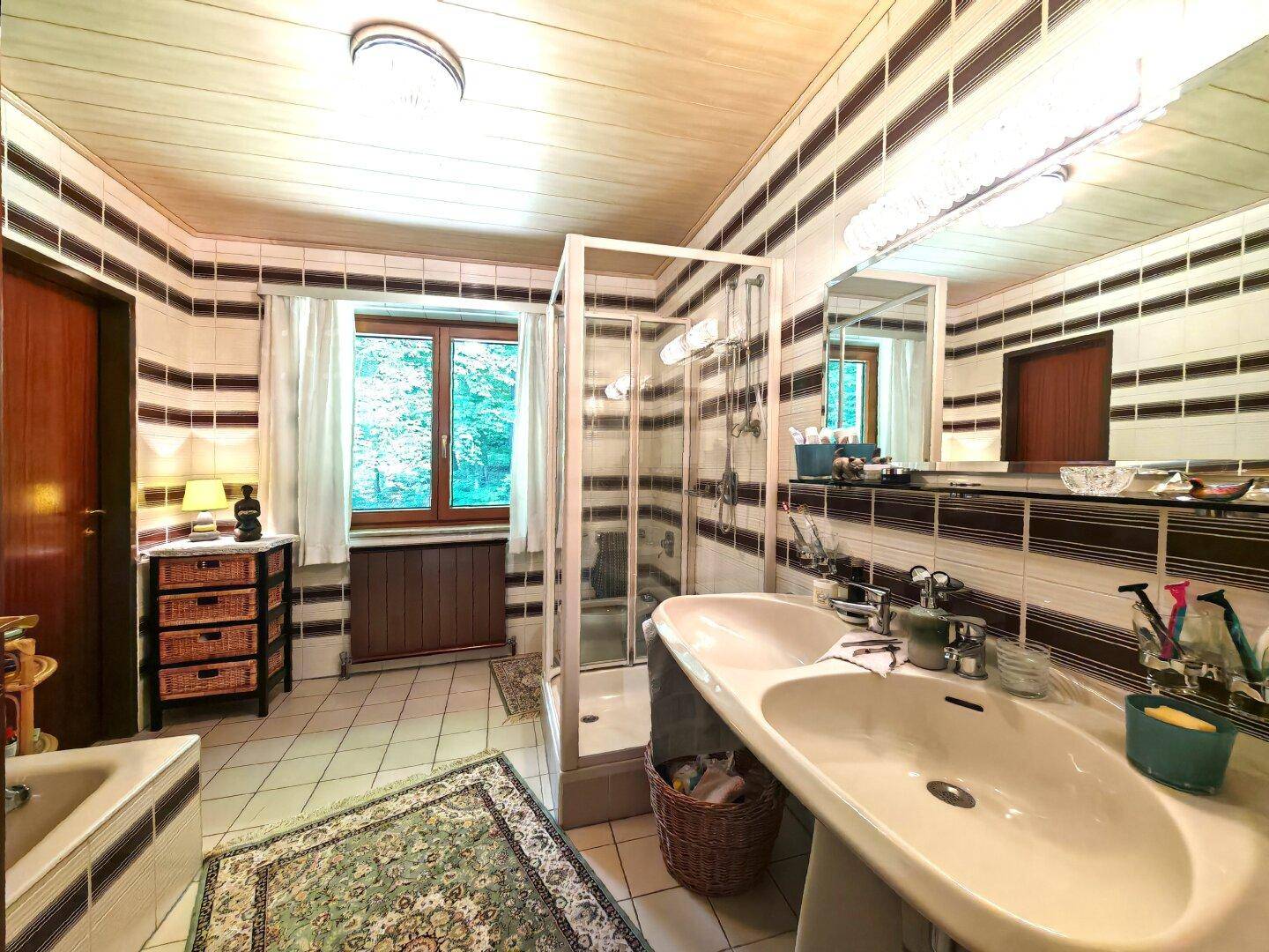 Geräumiges Badezimmer mit Doppelwaschbecken, Duschkabine, Badewanne und gestreiften Fliesen.
