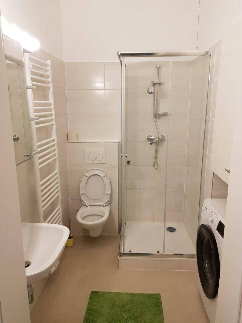 Modernes Badezimmer mit Dusche, WC, Waschbecken, beheiztem Handtuchhalter und Waschmaschine.