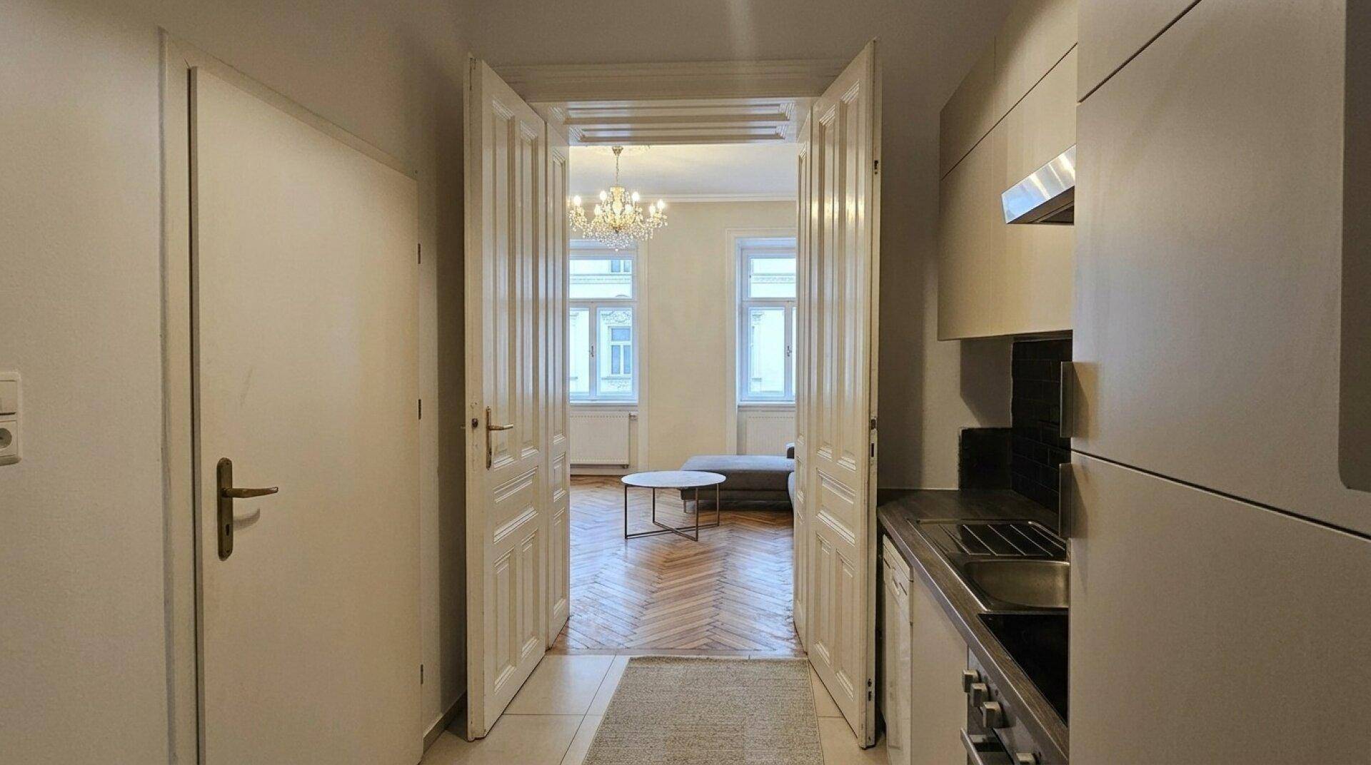 Flur mit Fliesenboden und Blick durch elegante Doppeltüren in das helle Wohnzimmer.