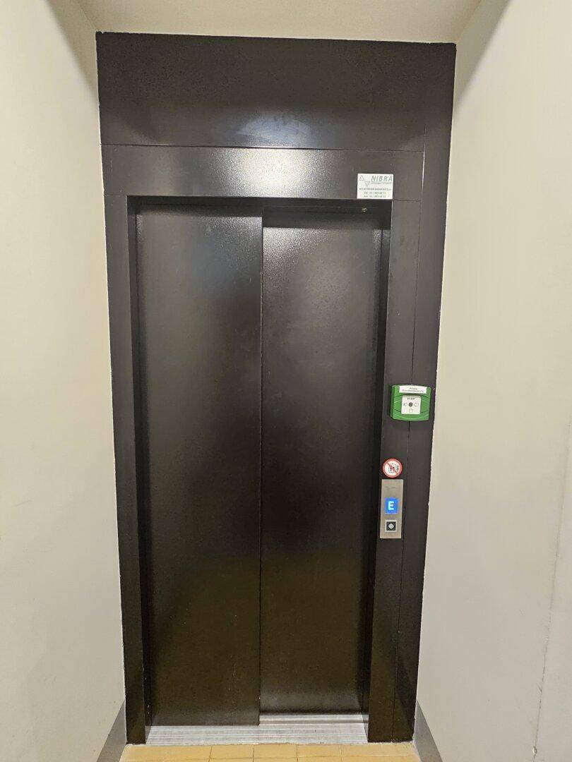 Moderner schwarzer Aufzug im Treppenhaus eines generalsanierten Altbaus.