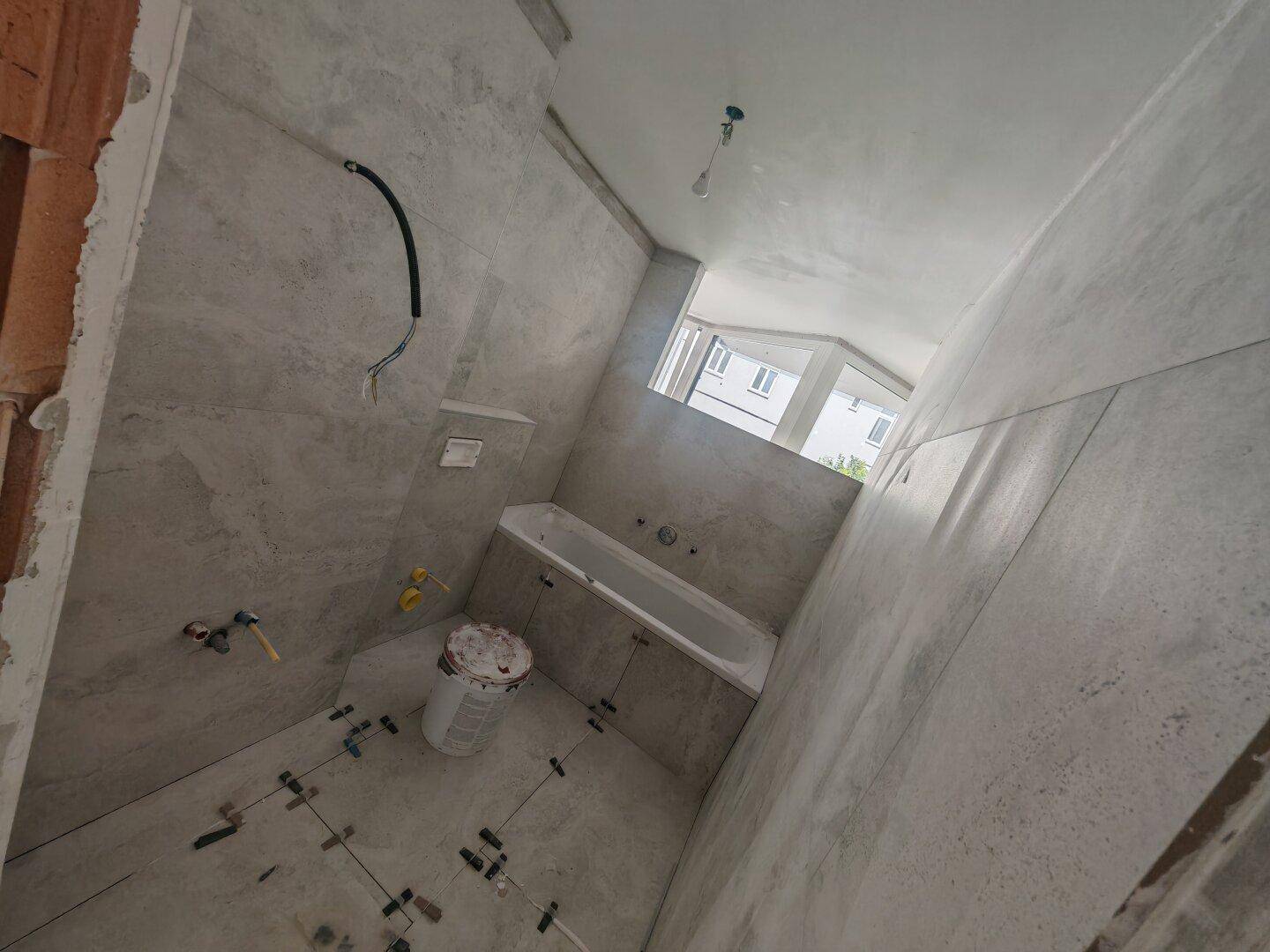 Badezimmer im Rohbau mit modernen Fliesen, eingebauter Badewanne und Fenster.