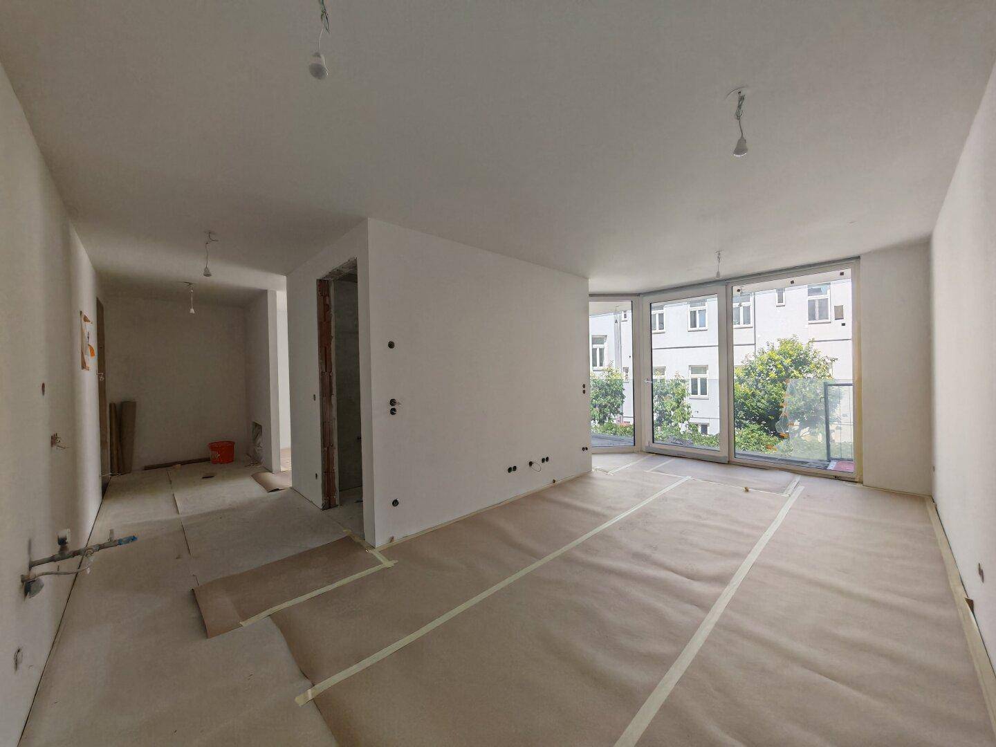 Geräumiger Innenraum im Rohbau mit großen Fenstern und Blick auf die umliegende Bebauung.