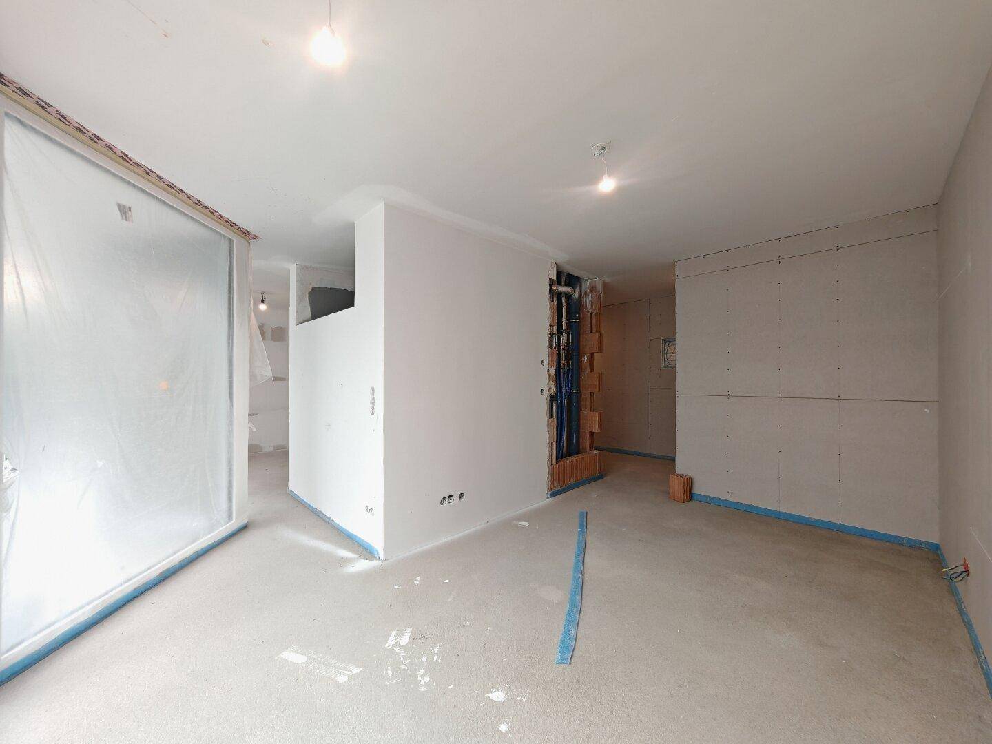 Unfertiger Innenraum mit freiliegenden Installationen und vorbereiteten Wänden für den Ausbau.