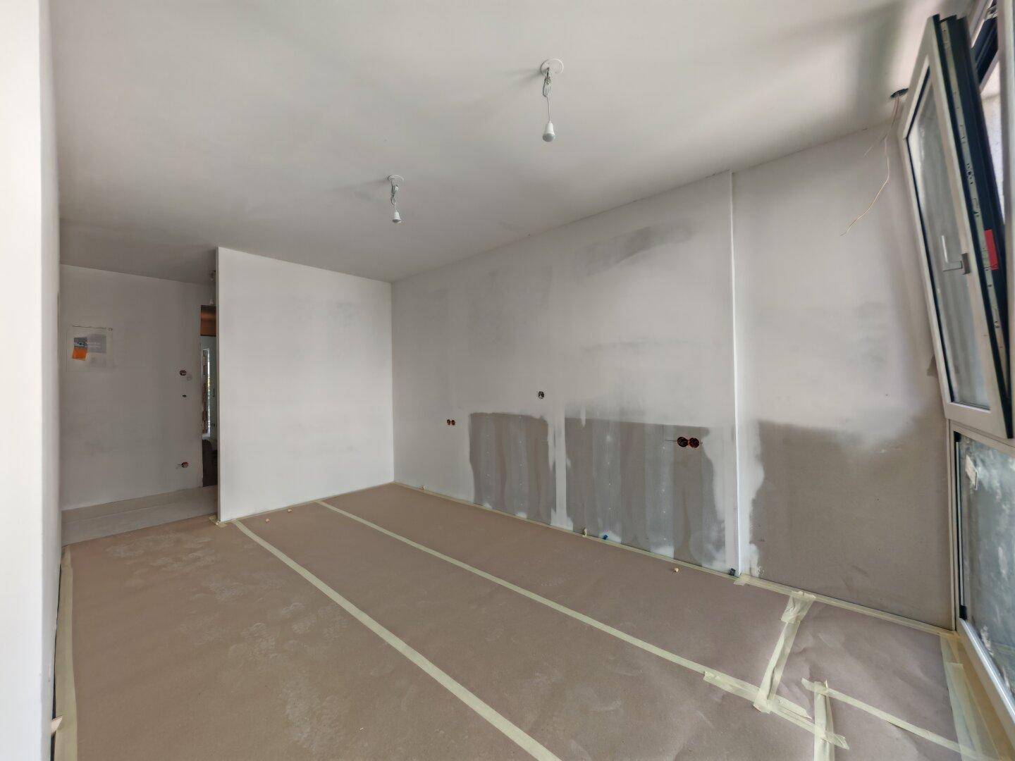 Heller Innenraum im Rohbau mit großen Fenstern und vorbereiteten Wänden für Installationen.