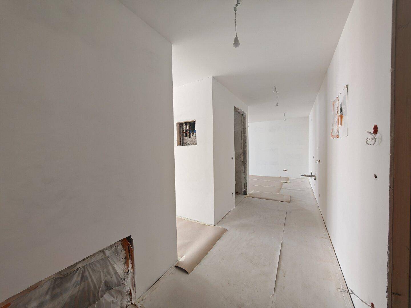 Langer, heller Flur im Rohbau mit weißen Wänden und unfertigem Betonboden.