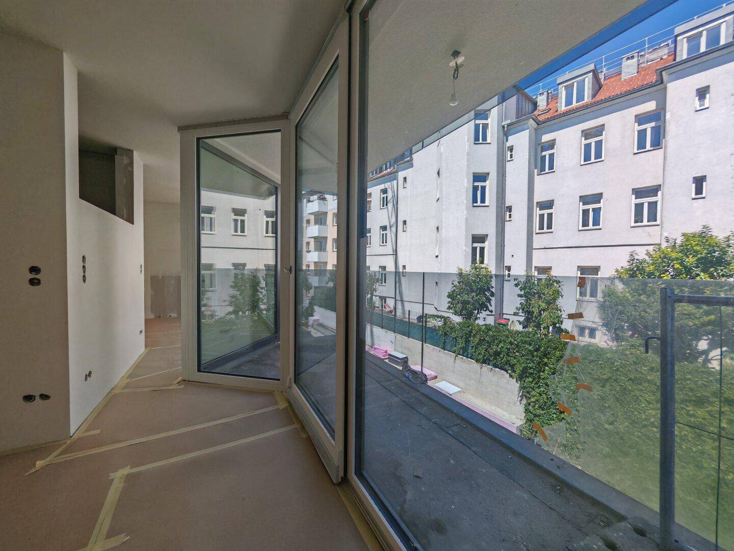 Heller Innenraum im Bau mit großen Glasfronten und Blick auf die Nachbargebäude und Vegetation.