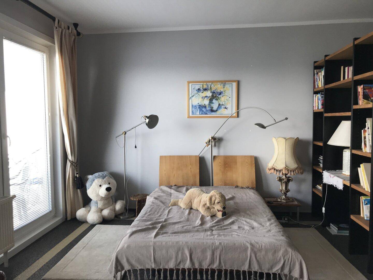 Gemütliches Schlafzimmer mit Bett, Bücherregal und großem Fenster für viel Tageslicht.