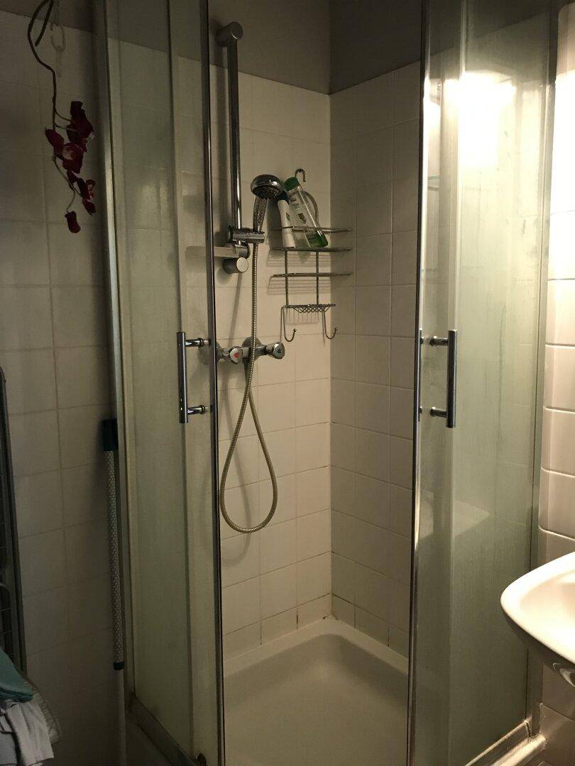 Duschkabine mit Glaswänden und Fliesen, ausgestattet mit Duschkopf und Ablage.