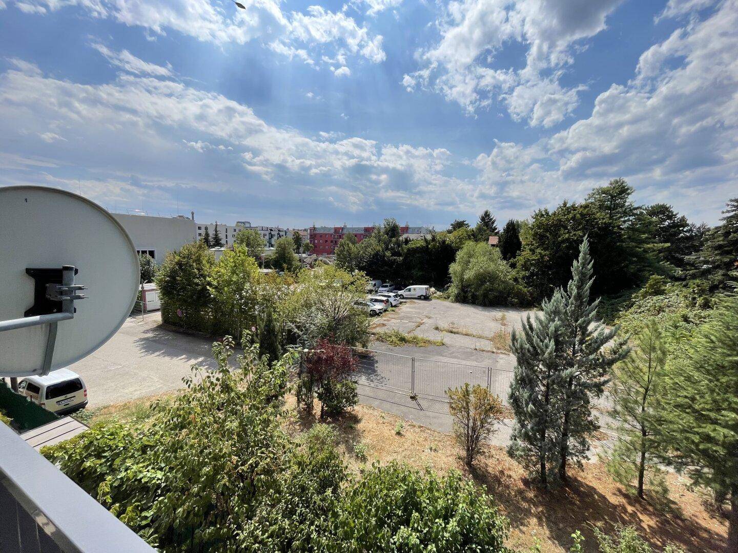 Weitläufiger Blick vom Balkon über Bäume, einen Parkplatz und die Umgebung.