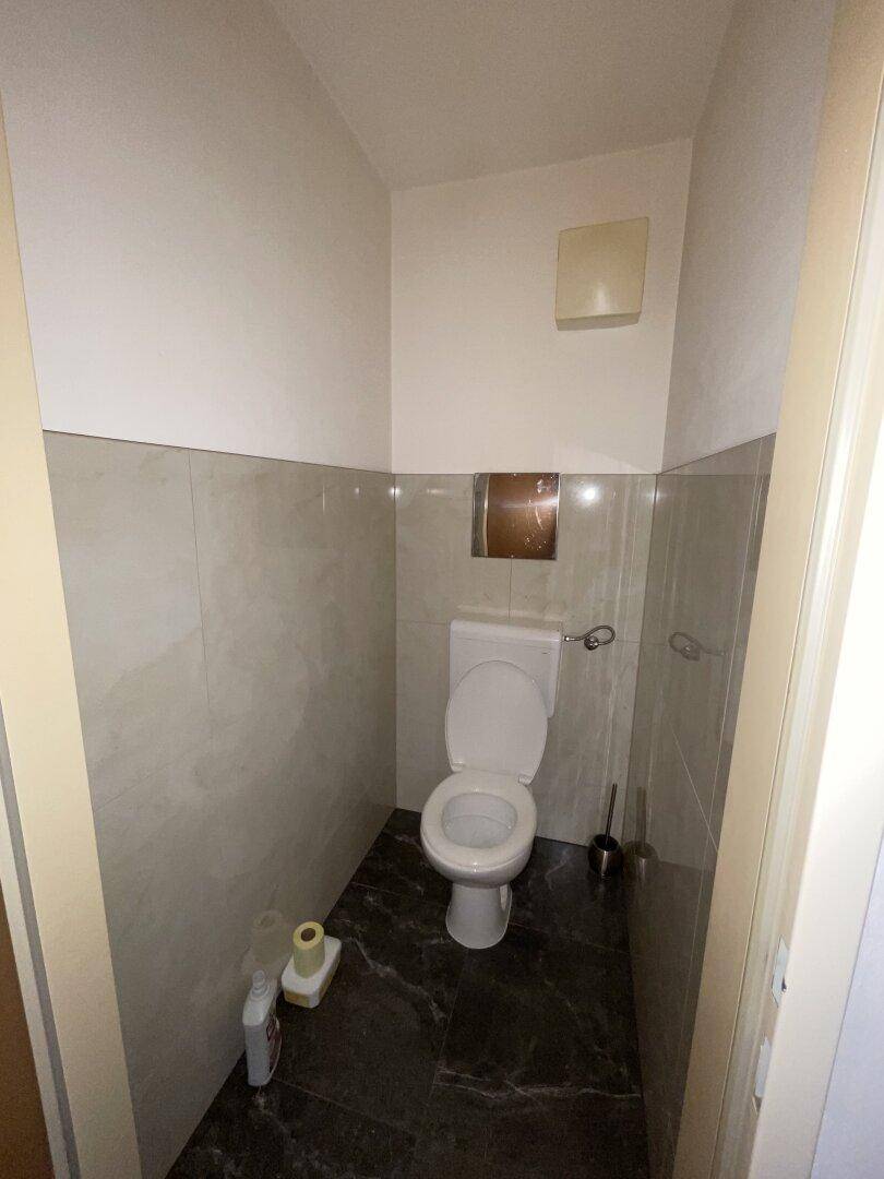 Separates WC mit Wandfliesen und dunklem Boden, funktional und sauber.