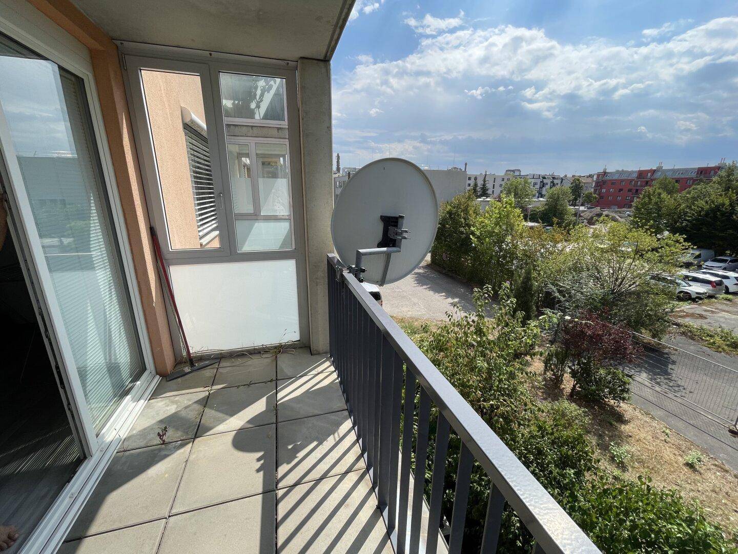 Balkon mit Satellitenschüssel und Blick auf Bäume sowie umliegende Gebäude.