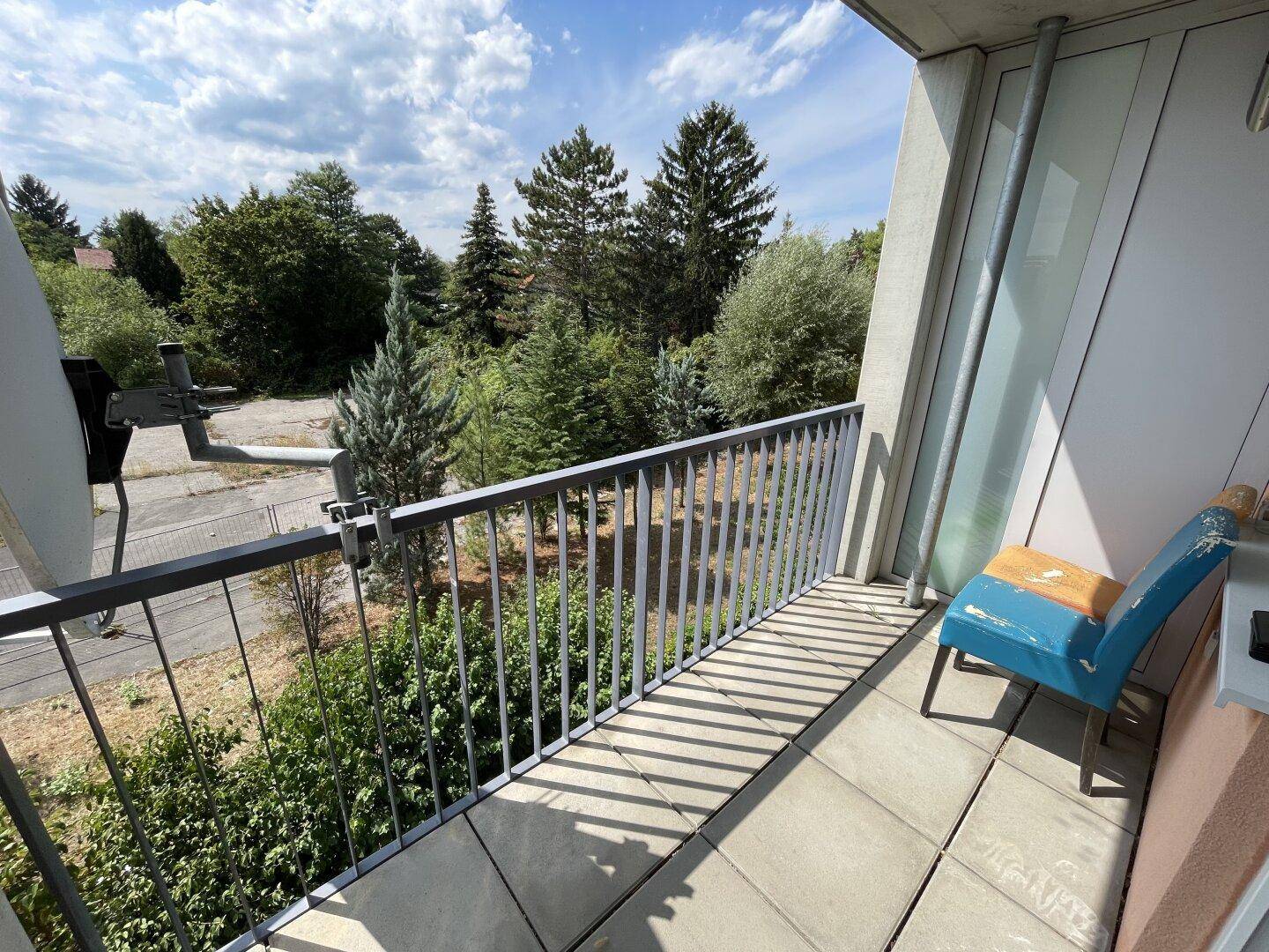 Balkon mit Fliesenboden und einem Stuhl, bietet einen weiten Blick ins Grüne.