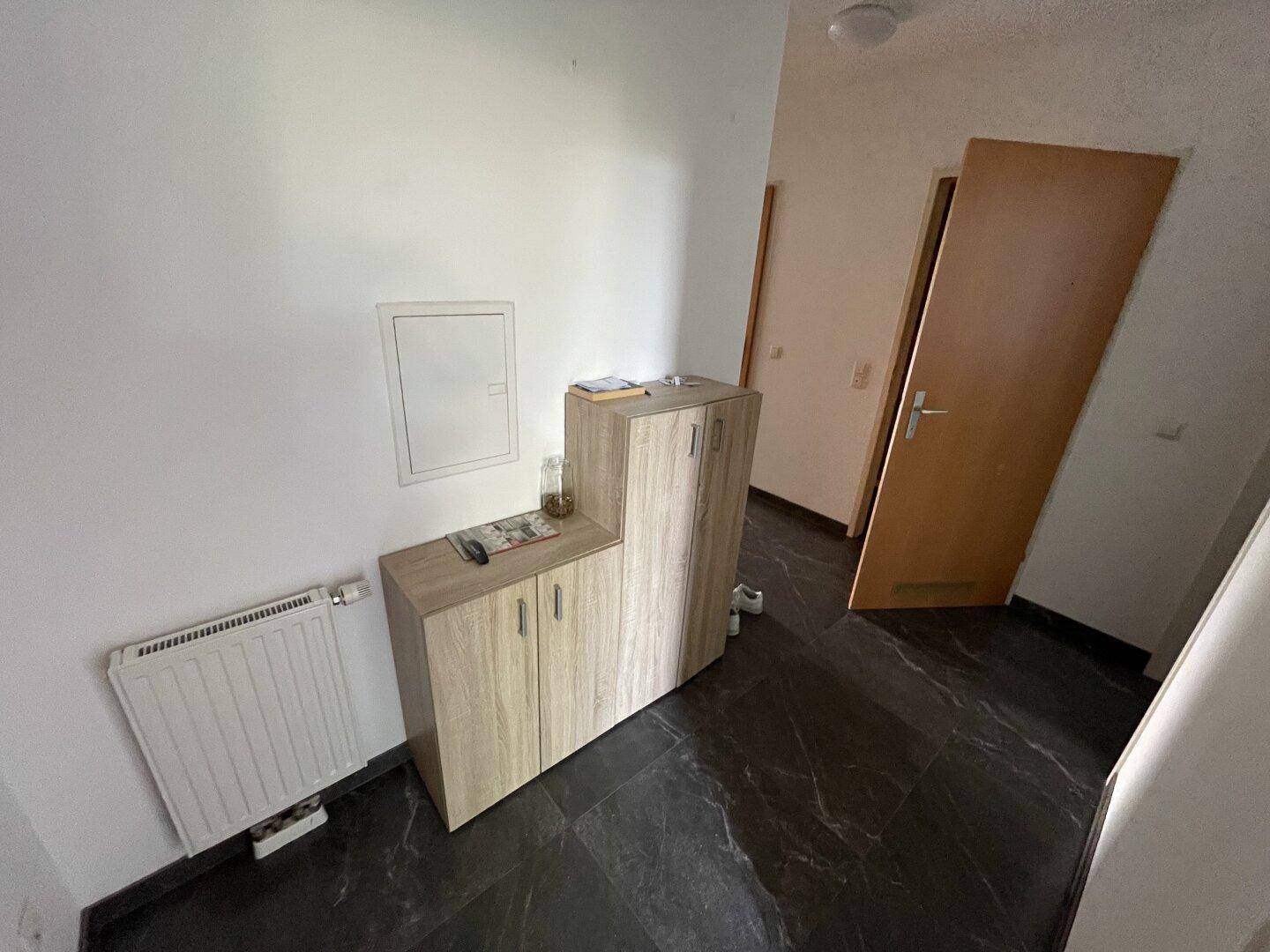 Heller Flur mit Heizkörper und praktischem Schrank, dunkler Fliesenboden.