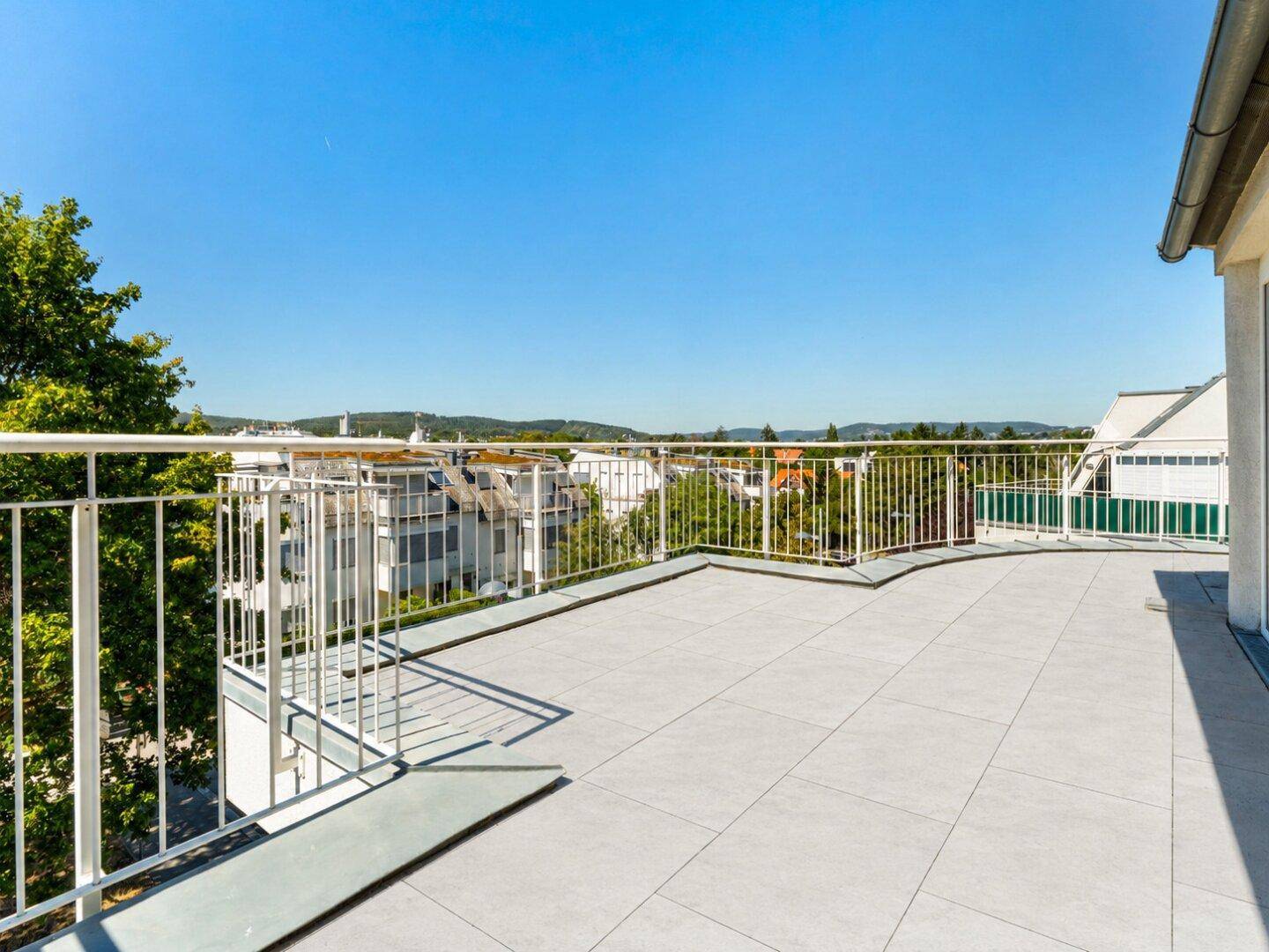 Weitläufige Dachterrasse mit Fliesenboden und Metallgeländer, bietet einen weiten Blick über die Umgebung.