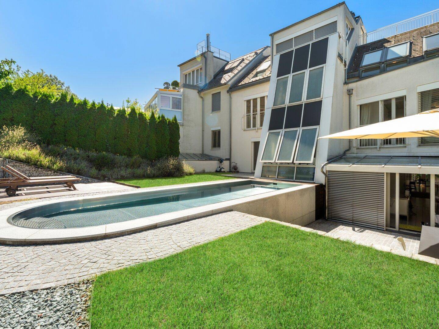 Langer, schmaler Pool im Gartenbereich einer modernen Villa mit Rasenfläche und Sonnenterrasse.