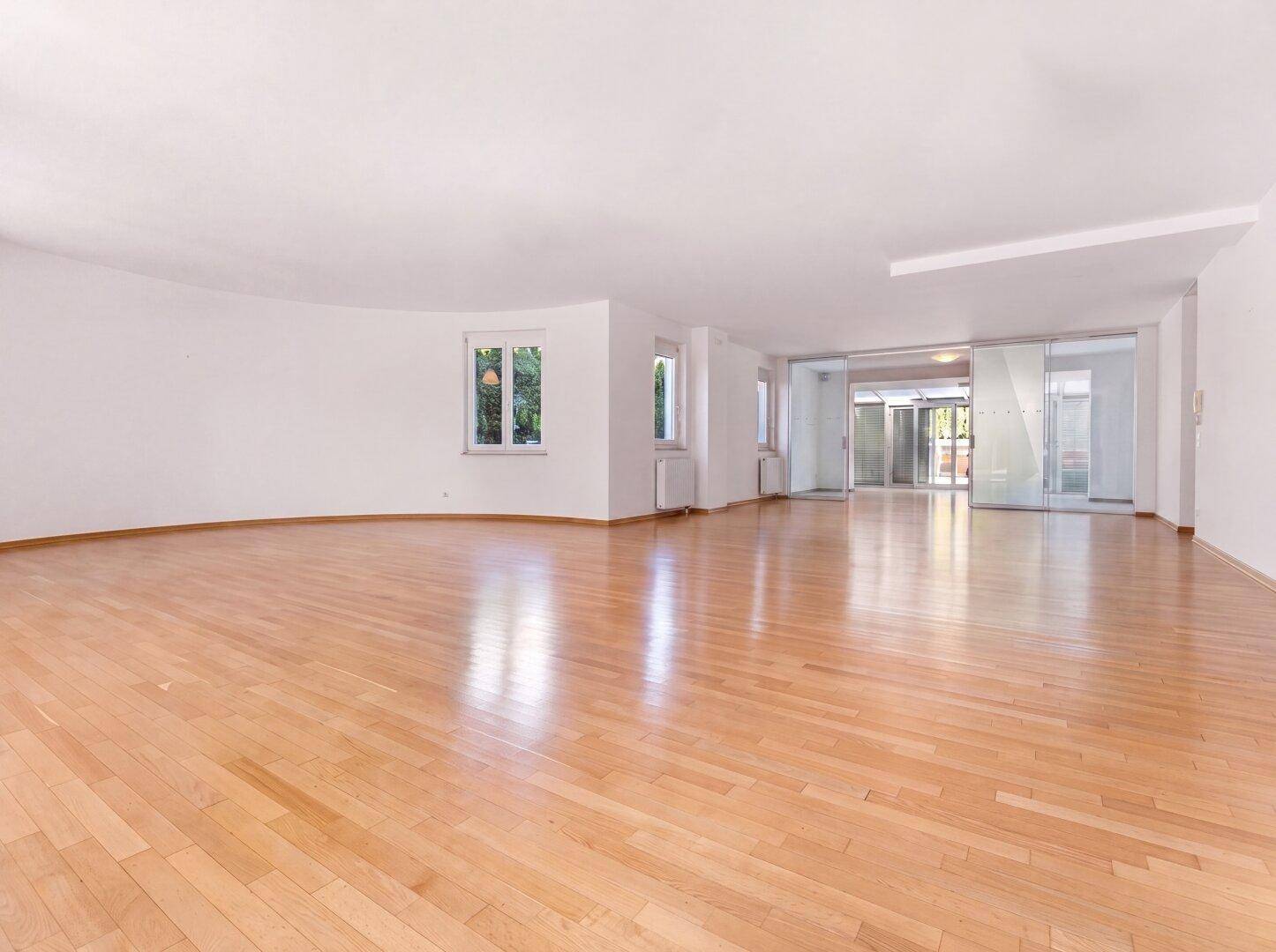 Offener Wohnbereich mit Parkettboden und Zugang zu einem hellen Eingangsbereich mit Glaswänden.