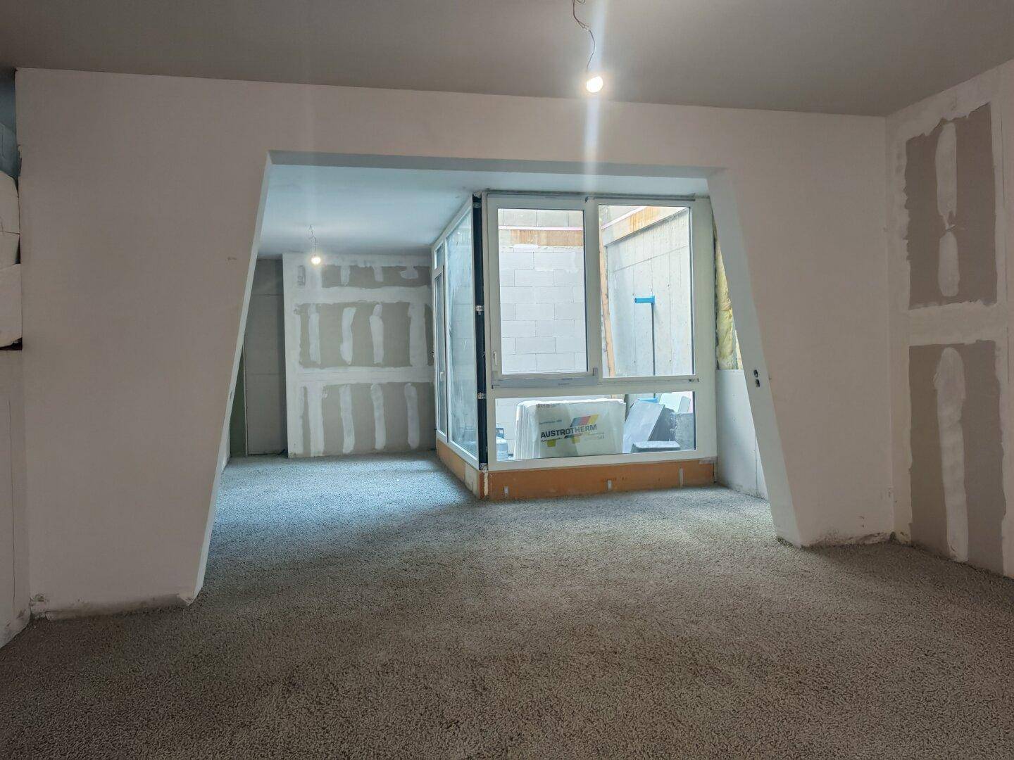 Unfertiger Innenraum mit großen Fenstern und Rohbauzustand, bereit für den weiteren Ausbau.