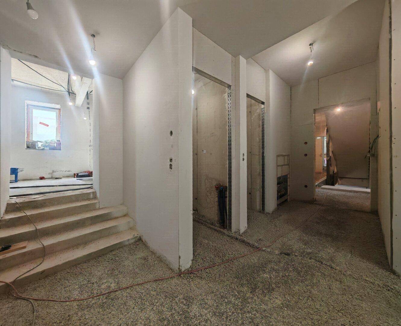 Baustelle mit unfertigen Wänden, einer Treppe und Rohinstallationen für Aufzüge oder Schächte.