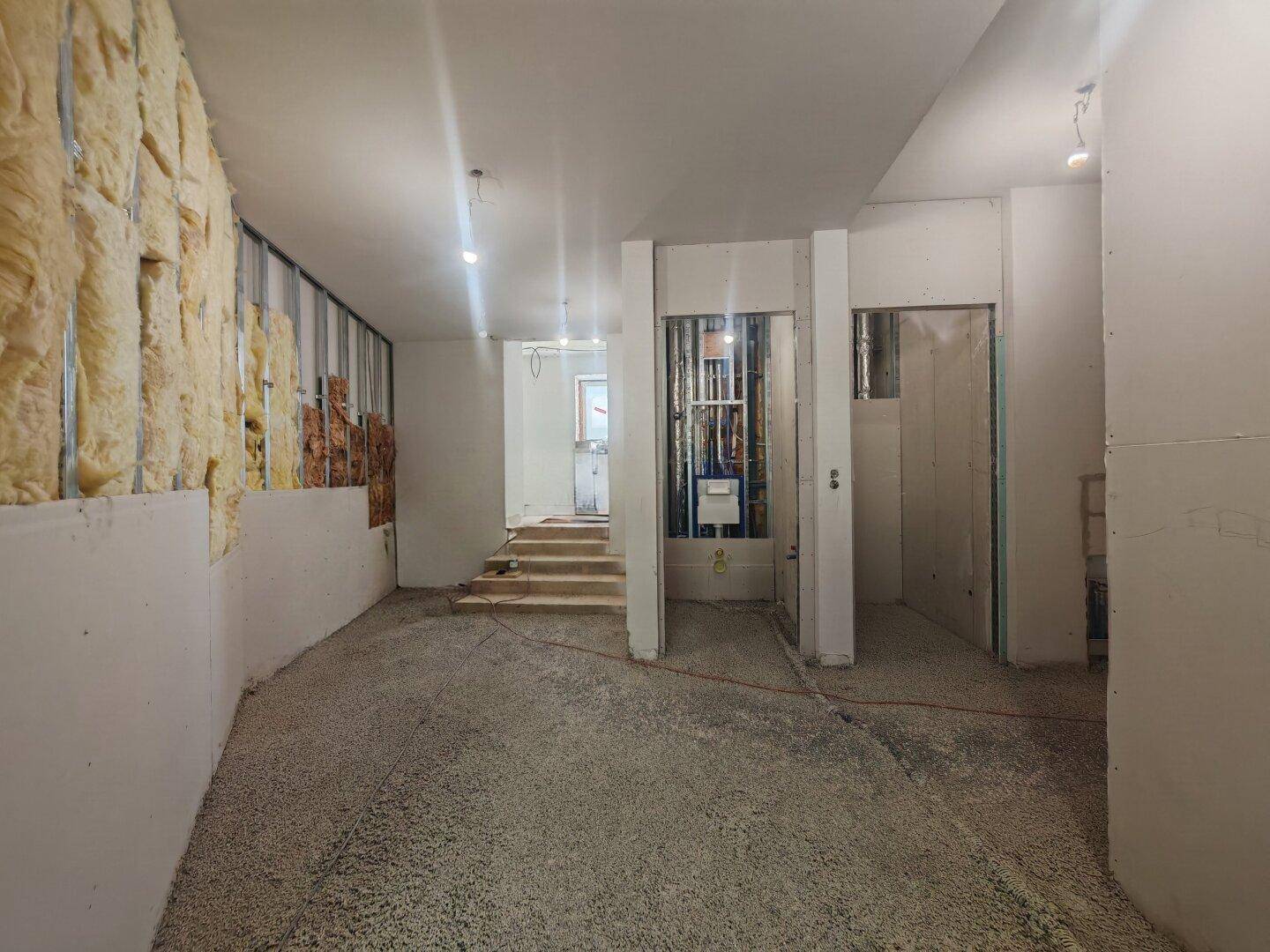 Rohbau eines Innenraums mit Dämmung an einer Wand und einem unfertigen Bodenbelag.