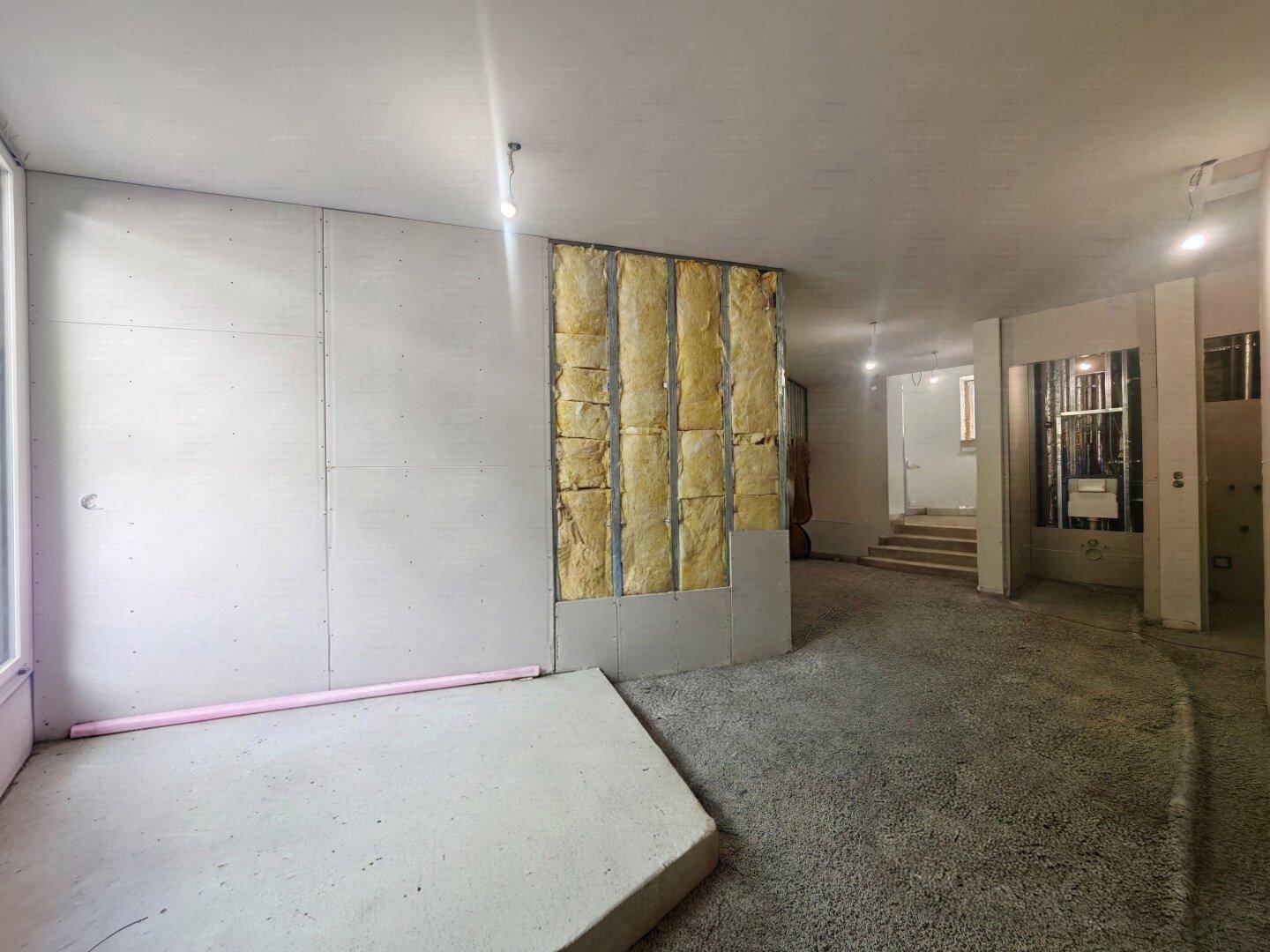 Unfertiger Innenraum mit Dämmung, einem Fenster und einem vorbereiteten Bodenbelag.