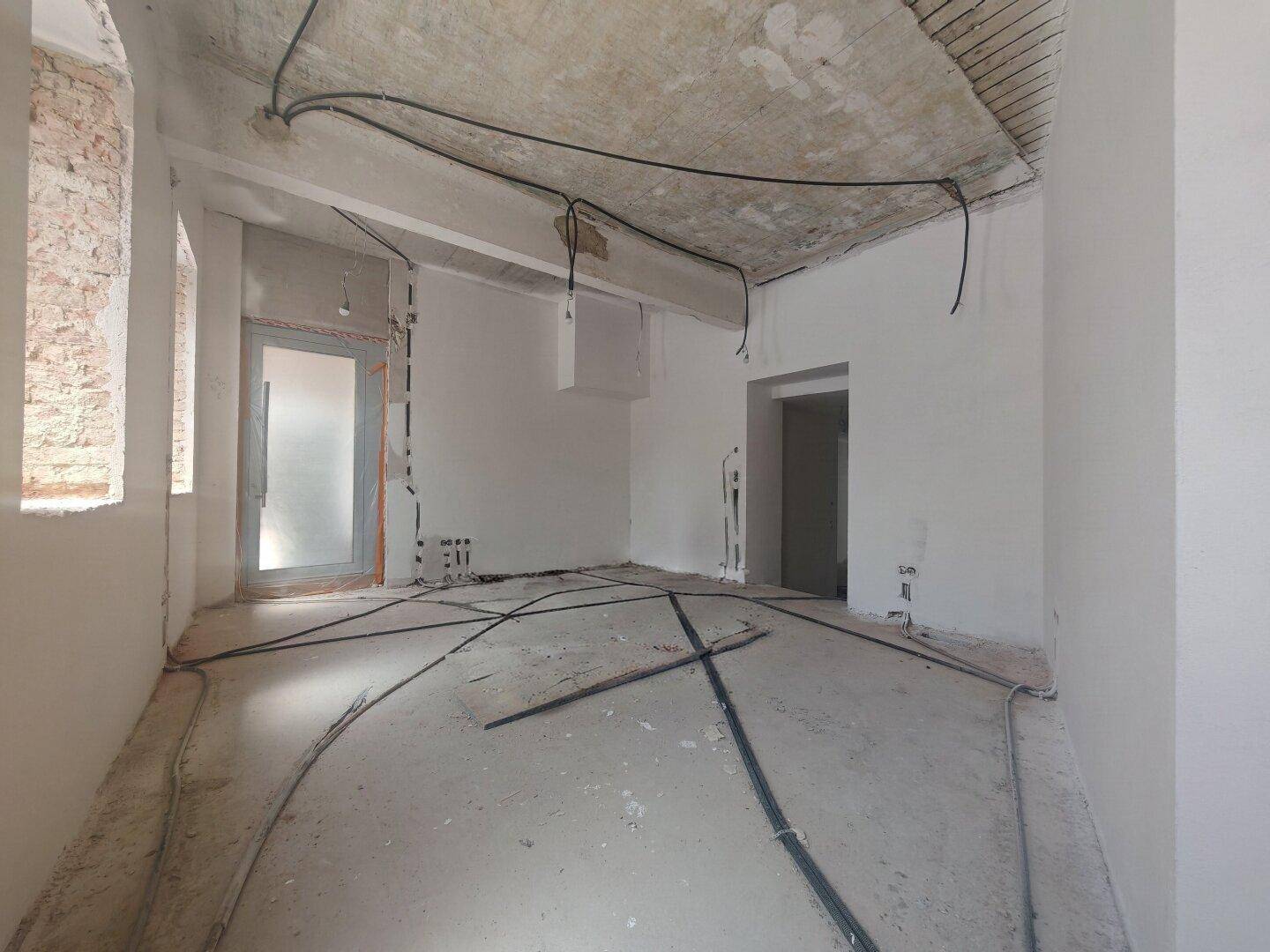Unfertiger Raum mit freiliegenden Kabeln an der Decke und Wänden, bereit für den Ausbau.