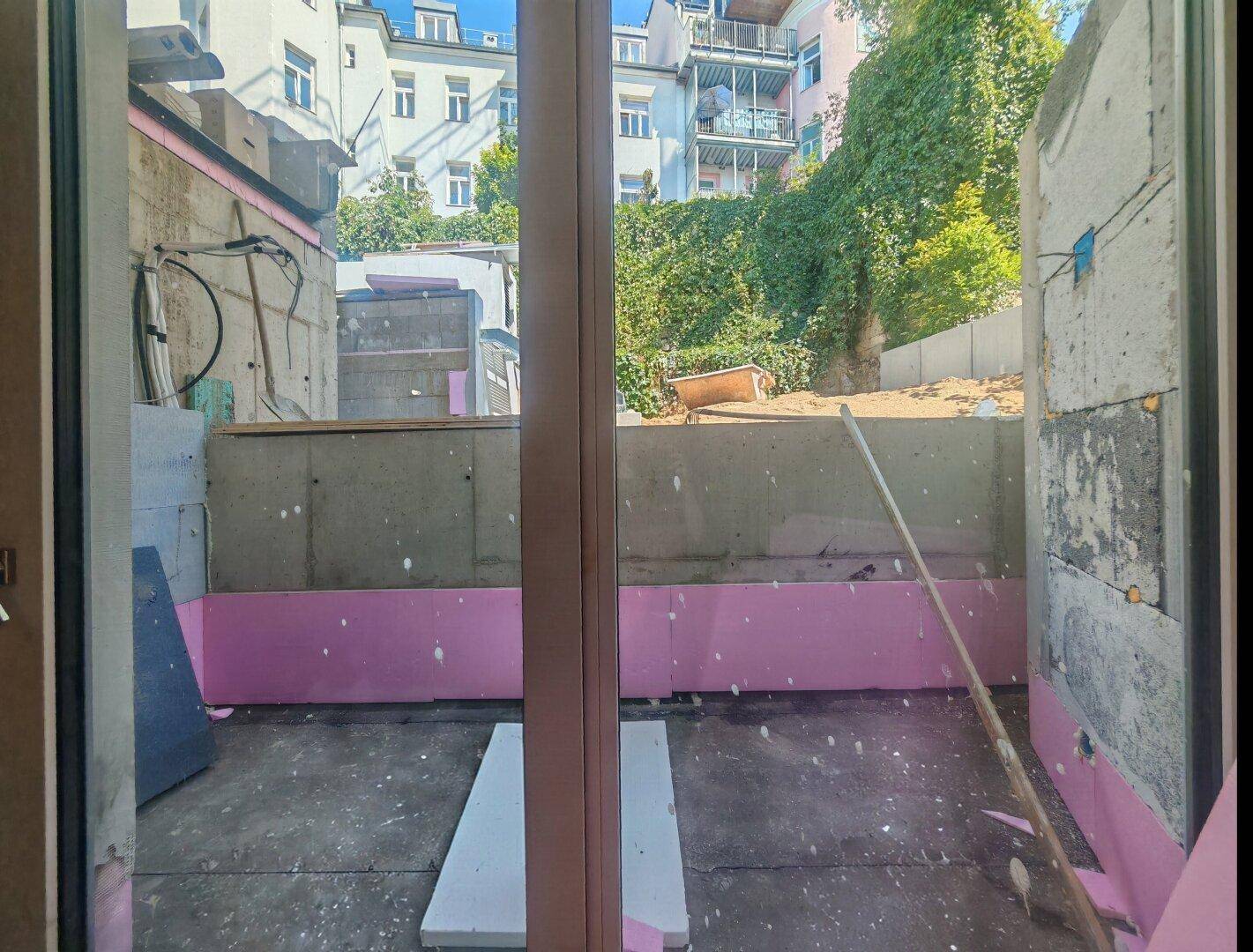 Blick aus einem Fenster auf eine Baustelle im Außenbereich mit Dämmmaterial und angrenzenden Gebäuden.