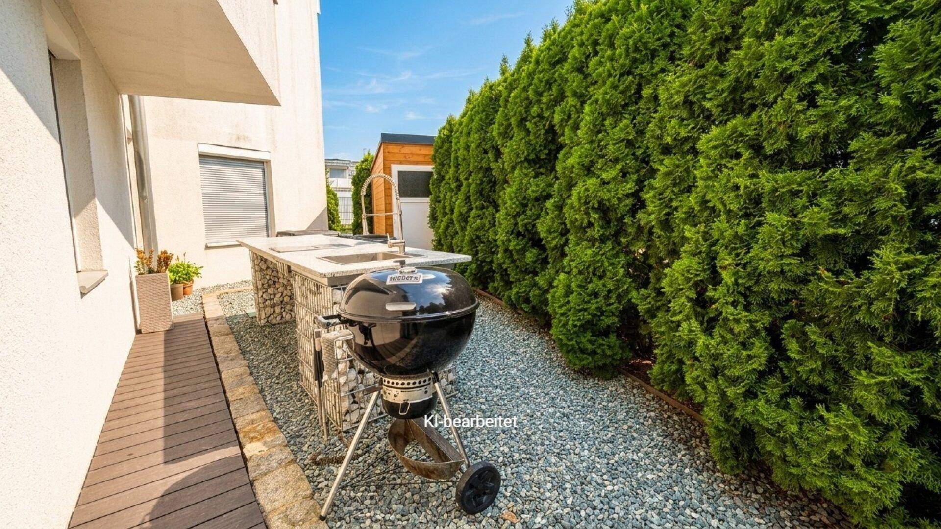 Außenküche mit Grill und Arbeitsfläche im Gartenbereich, umgeben von einer hohen Hecke.
