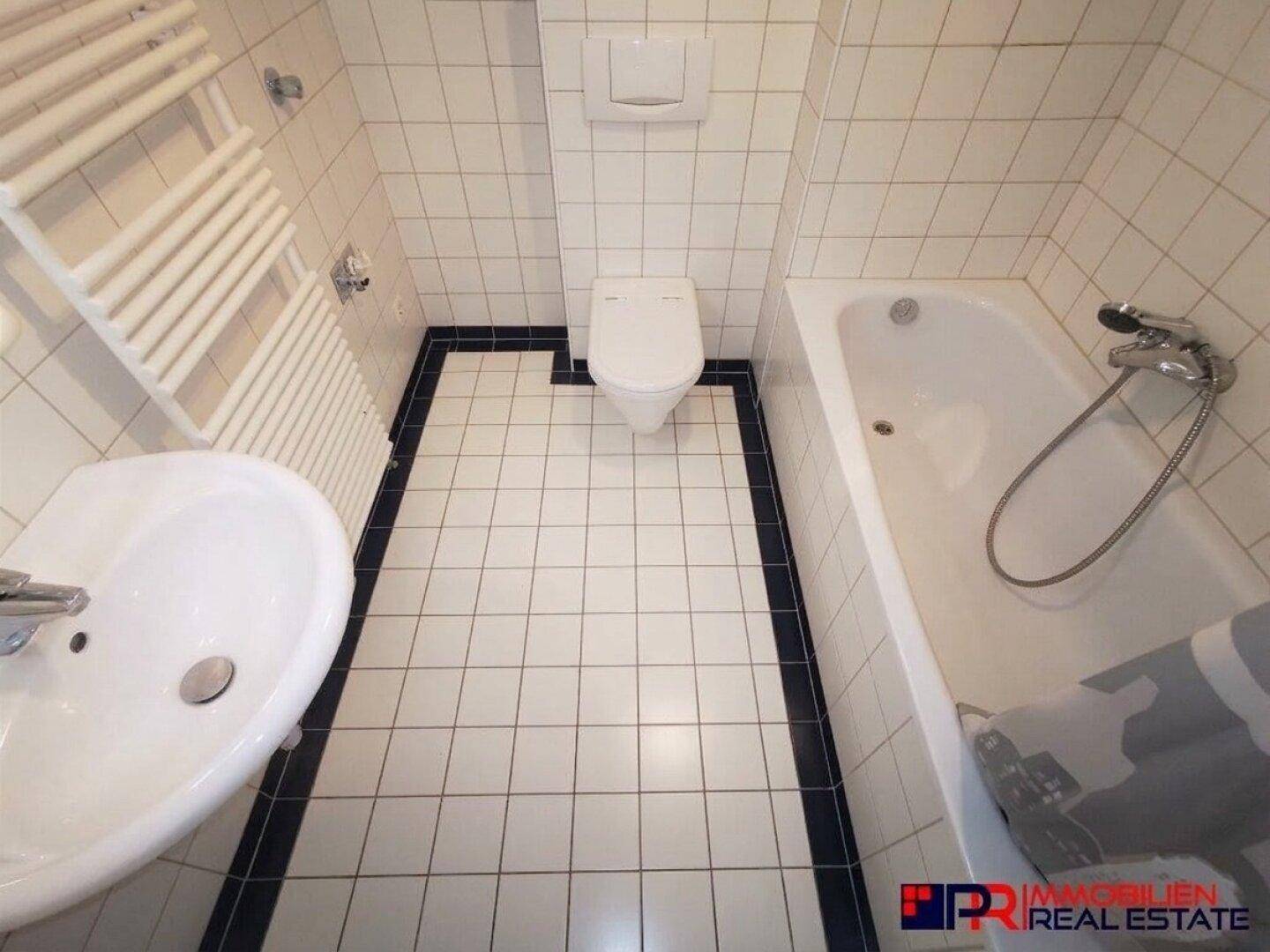 Badezimmer mit Badewanne, Toilette und Waschbecken, gefliest in Weiß und Schwarz, funktional.