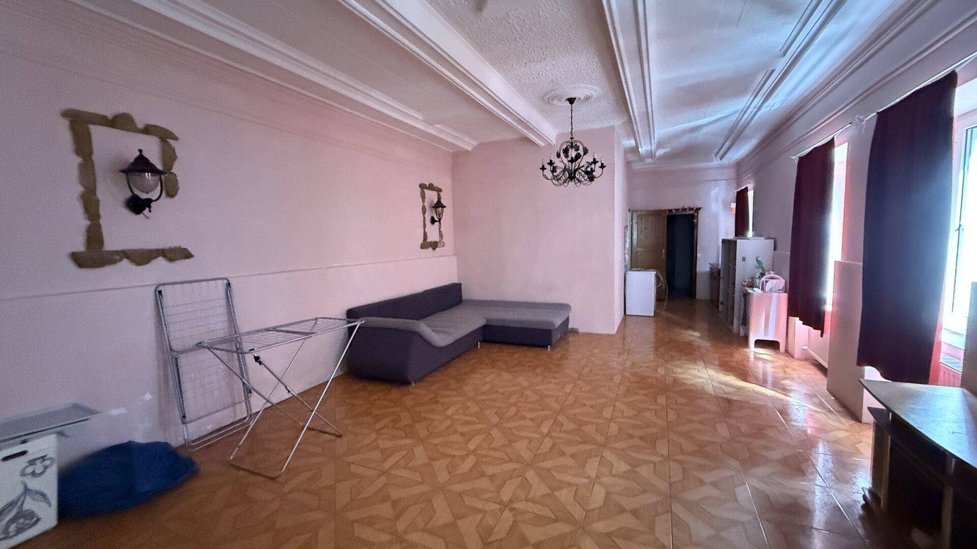 Geräumiges Wohnzimmer mit rosa Wänden, gemustertem Fliesenboden und einfacher Einrichtung.