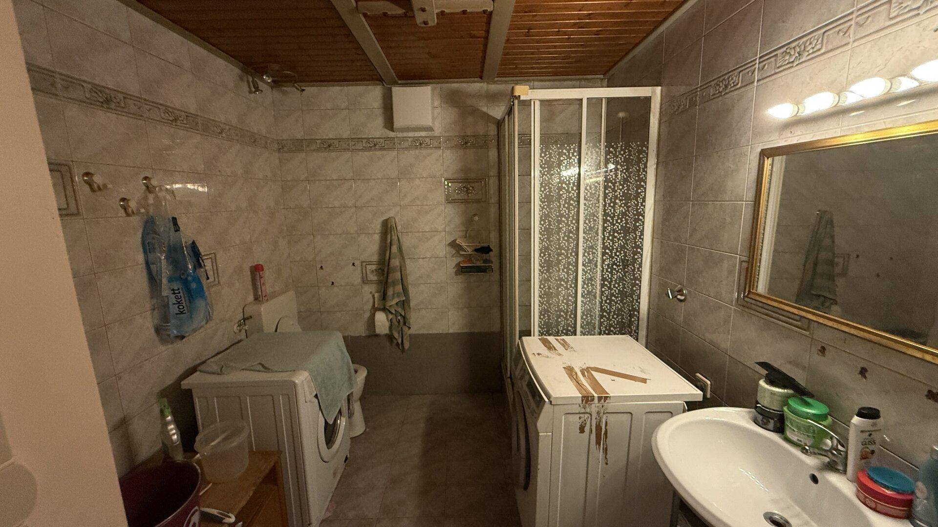 Älteres Badezimmer mit Duschkabine, WC, Waschtisch und gefliesten Wänden.