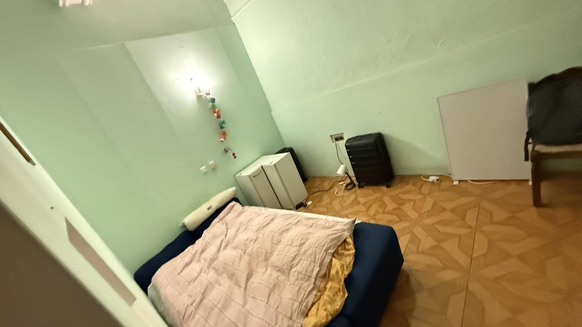Schlafzimmer mit grünen Wänden, gemustertem Fliesenboden und einem einfachen Bett.