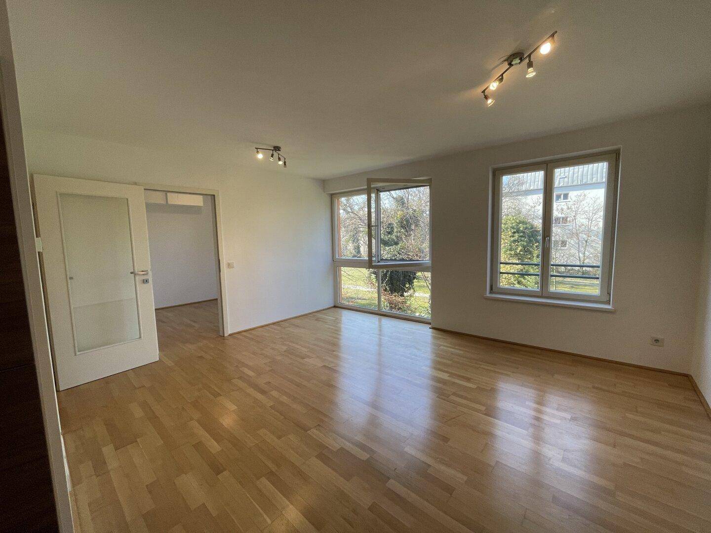 Helles Wohnzimmer mit Parkettboden und großen Fenstern, die einen Blick ins Grüne bieten.