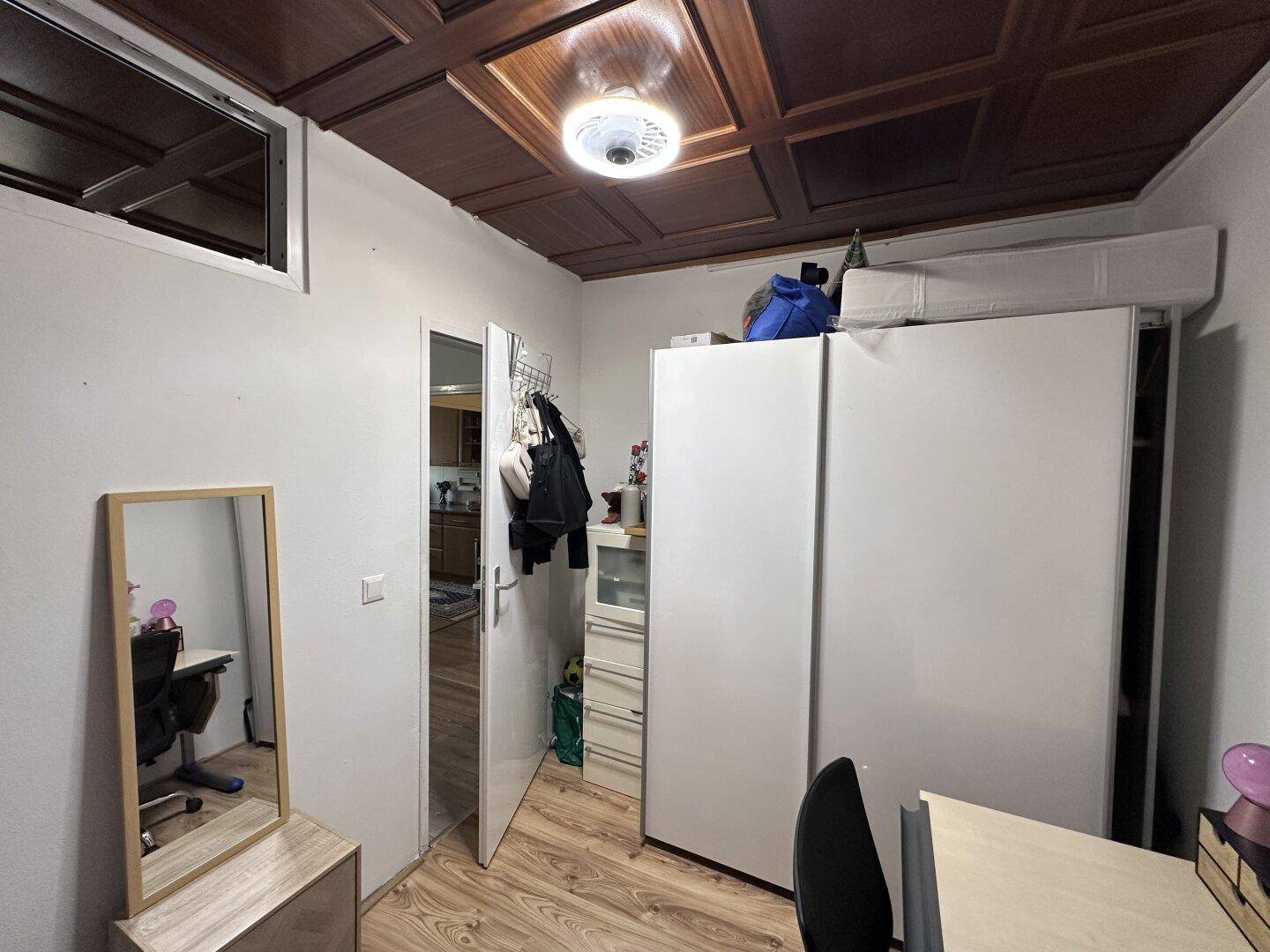 Schlafzimmer mit Kleiderschrank, Schreibtisch und einer charakteristischen Holzdecke.