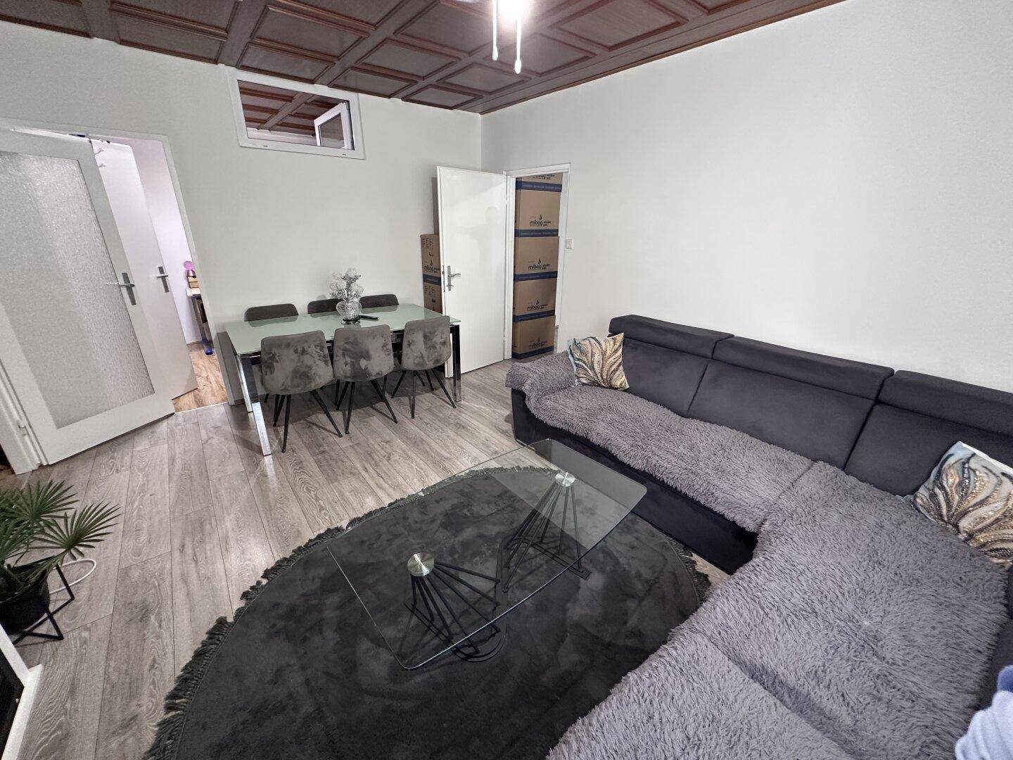 Gemütlicher Wohn-Essbereich mit modernem Esstisch und dunklem Ecksofa unter der Holzdecke.