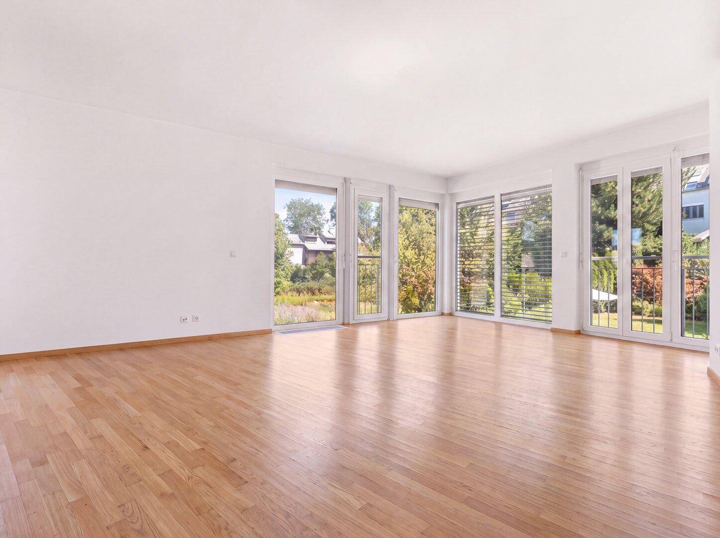 Lichtdurchfluteter Wohnraum mit Holzboden und bodentiefen Fenstern, die viel Tageslicht hereinlassen.
