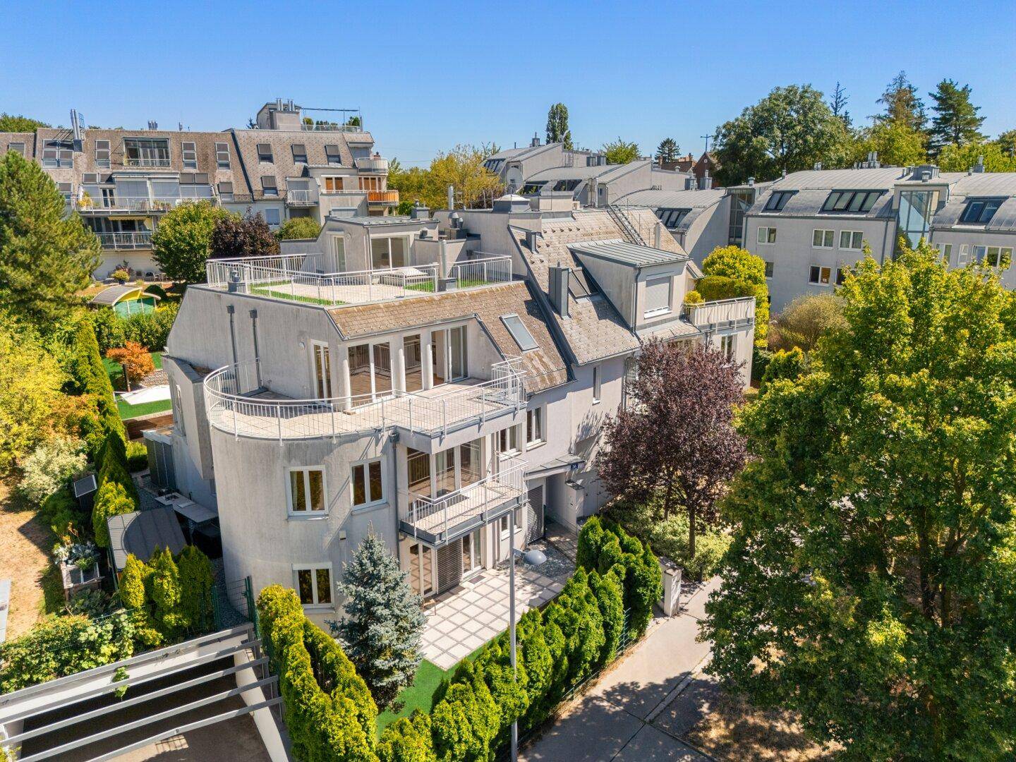 Moderne Wohnanlage mit mehreren Balkonen und Dachterrassen, umgeben von viel Grün und Bäumen.