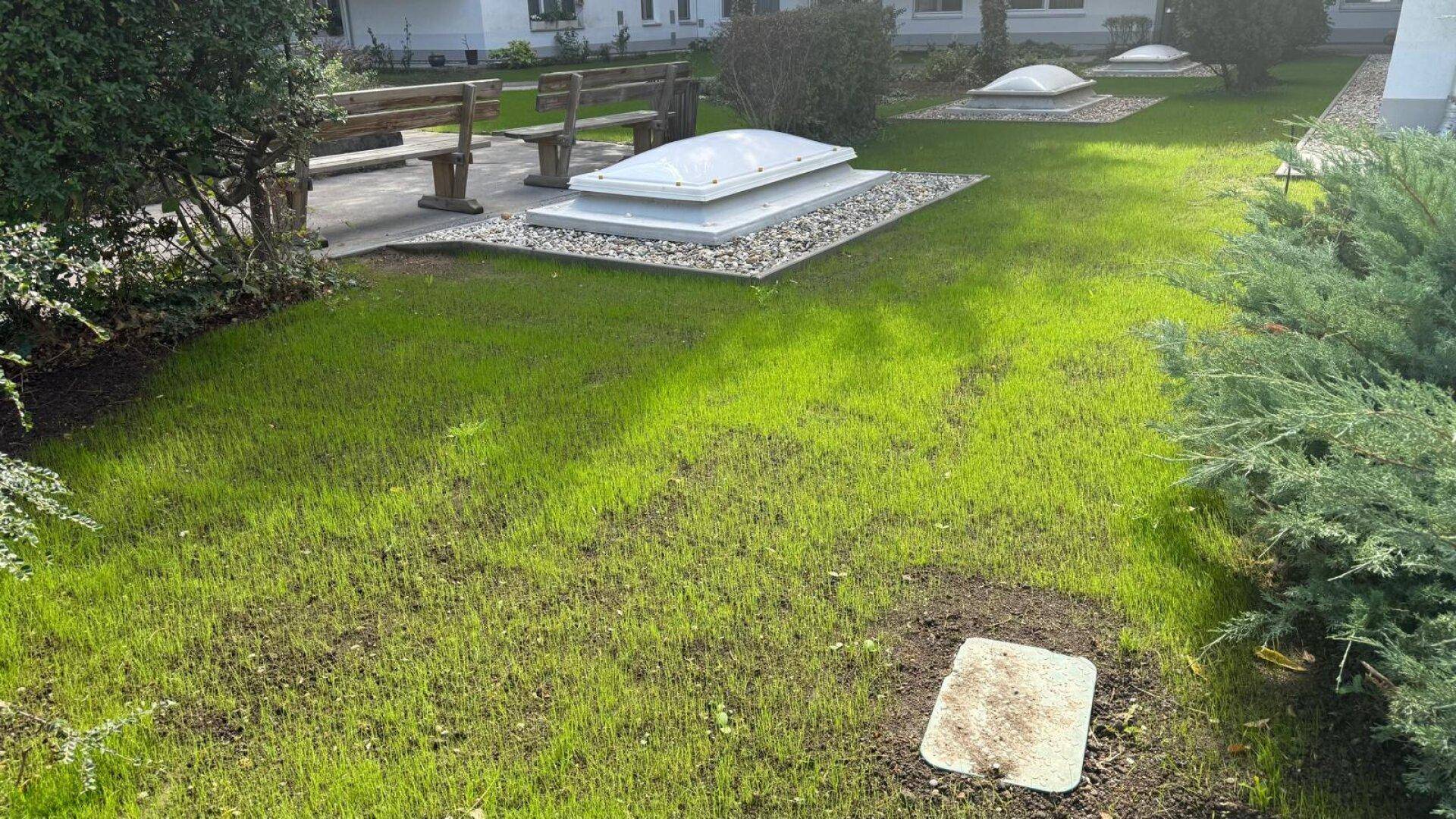 Gemeinschaftsgarten mit Sitzbänken, Rasenfläche und Lichtkuppeln für den Keller.