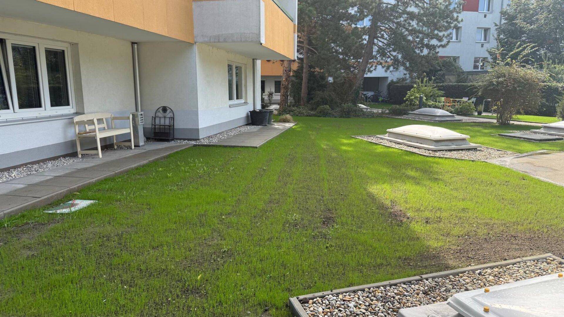 Gepflegte Gartenanlage neben dem Gebäude mit Sitzbänken und Lichtkuppeln.