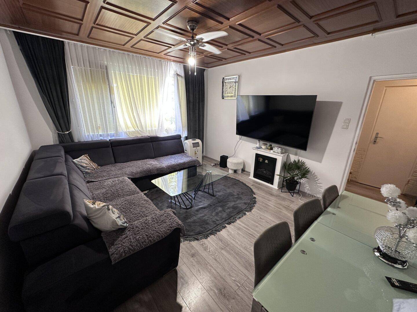 Heller Wohn-Essbereich mit großem Ecksofa, Fernseher und charakteristischer Holzdeckenvertäfelung.