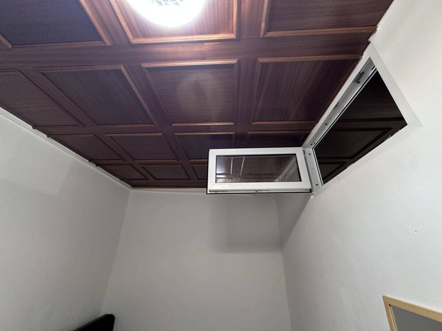 Detailansicht der Holzdeckenvertäfelung und eines hoch angebrachten Fensters.