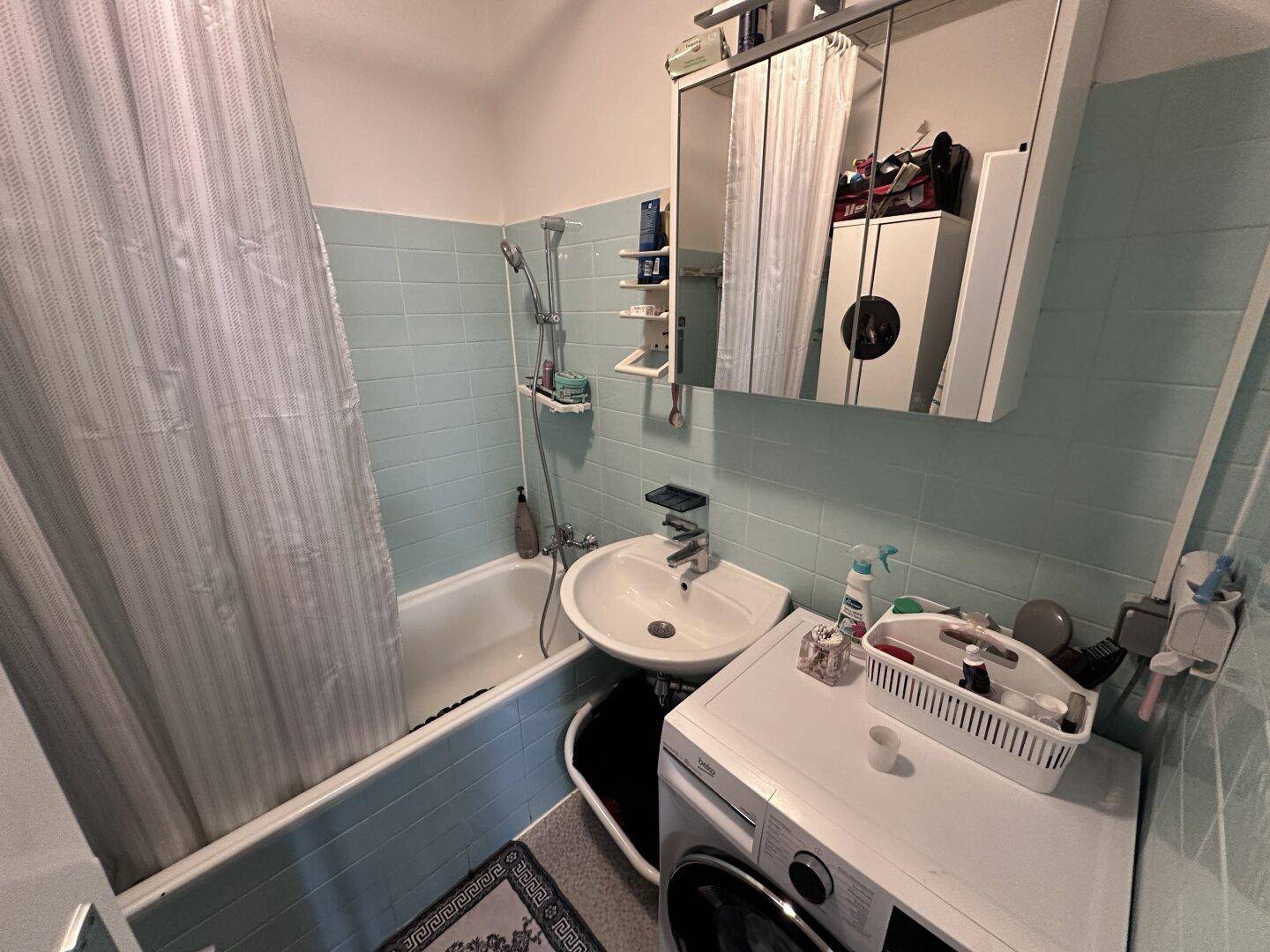 Badezimmer mit Badewanne, Duschvorhang, Waschbecken und Waschmaschine.