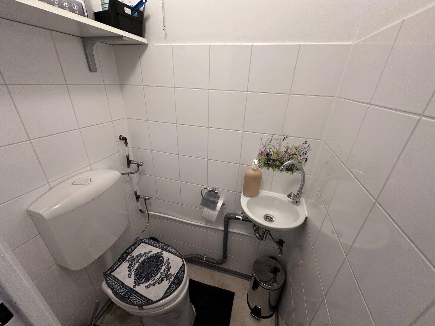Kleines Gäste-WC mit Toilette, kleinem Waschbecken und weißen Fliesen.