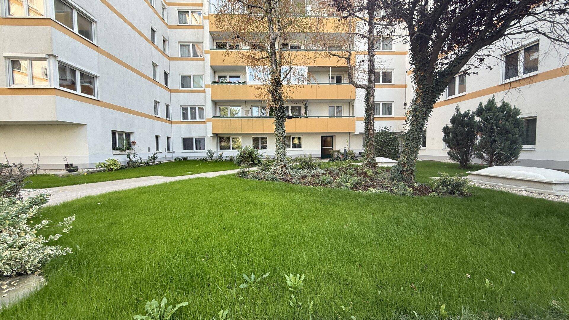 Gepflegte Grünfläche vor der Wohnanlage mit Bäumen und Balkonen an der Fassade.
