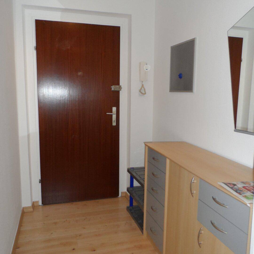 Heller Eingangsbereich mit Holztür, kleinem Schrank und Spiegel, einladend gestaltet.