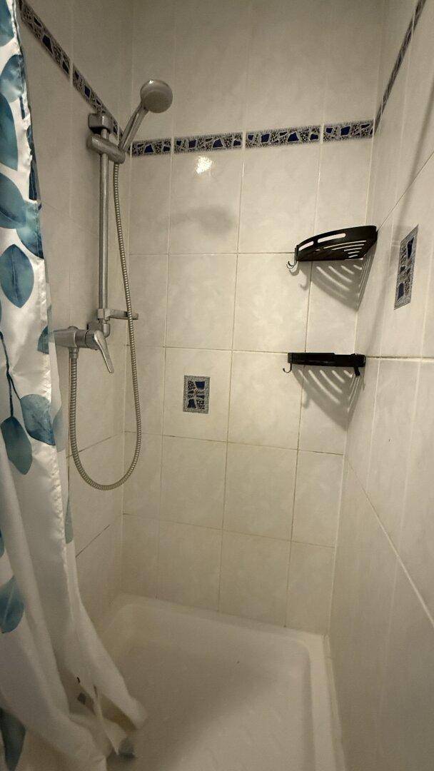 Duschbereich im Badezimmer mit Fliesen und Duschvorhang, sauber und funktional.