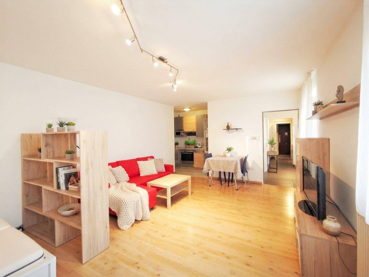 Offener Wohn- und Essbereich mit rotem Sofa, Esstisch und Blick auf die Küchenzeile.