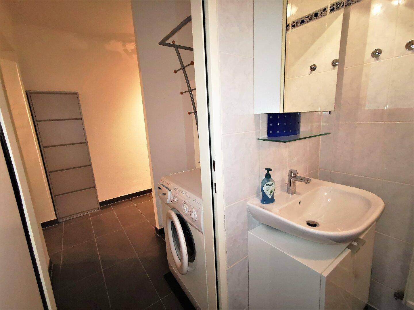 Kleiner Waschraum mit Waschbecken, Spiegelschrank und Waschmaschine.